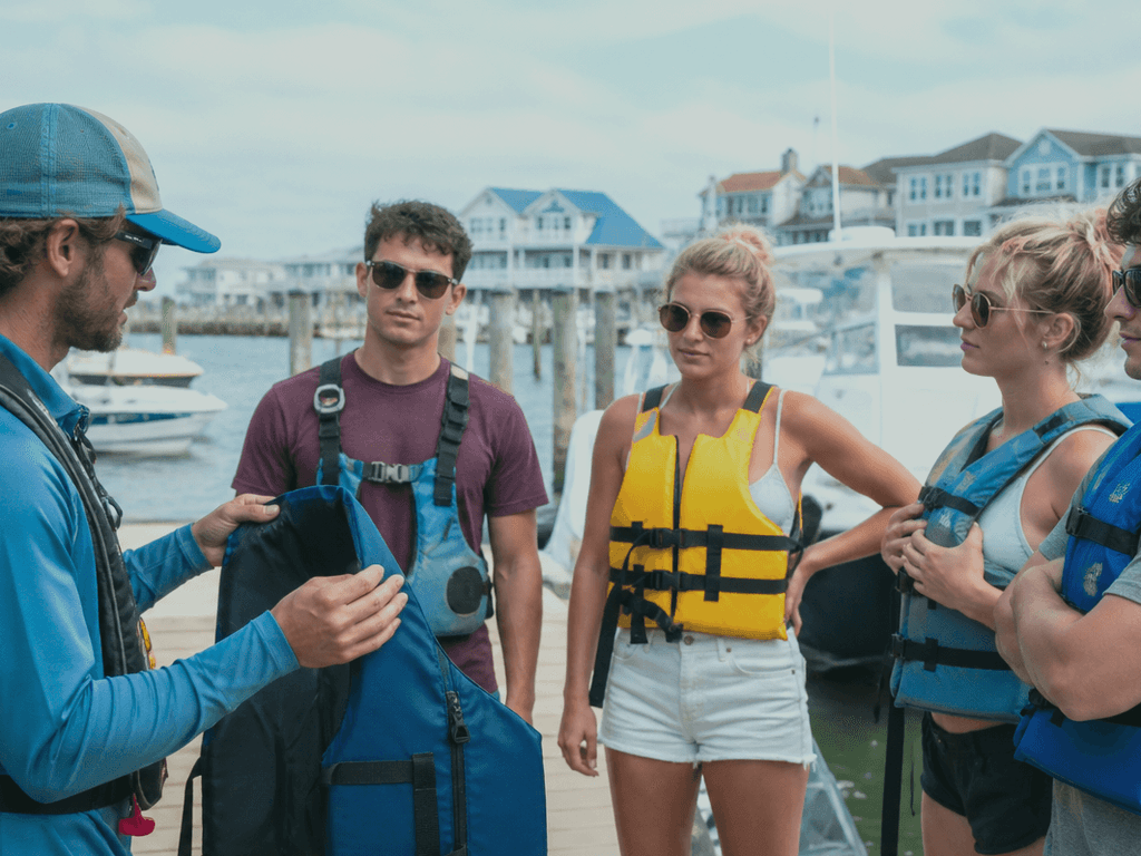 Hands pointing to life jackets and a throw bag during a boat safety briefing at an Ocean City Maryland marina