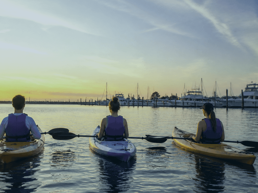 Friends checking wind and life jackets before a sunset paddle launch on Assawoman Bay — Ocean City, Maryland