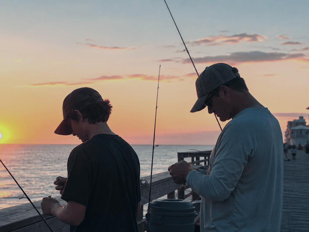 Two fishing rods on pier rail at dawn with teenager learning to bait hook — Ocean City, Maryland