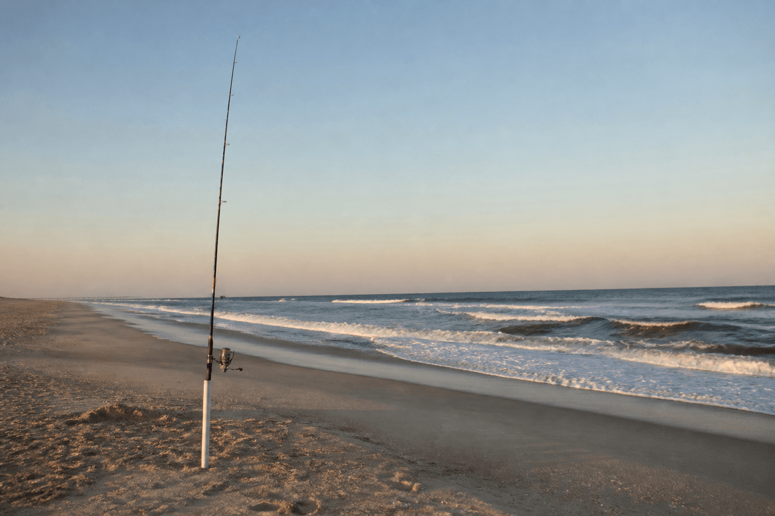 Surf angler casting at dawn on an Ocean City beach with chop and empty sand