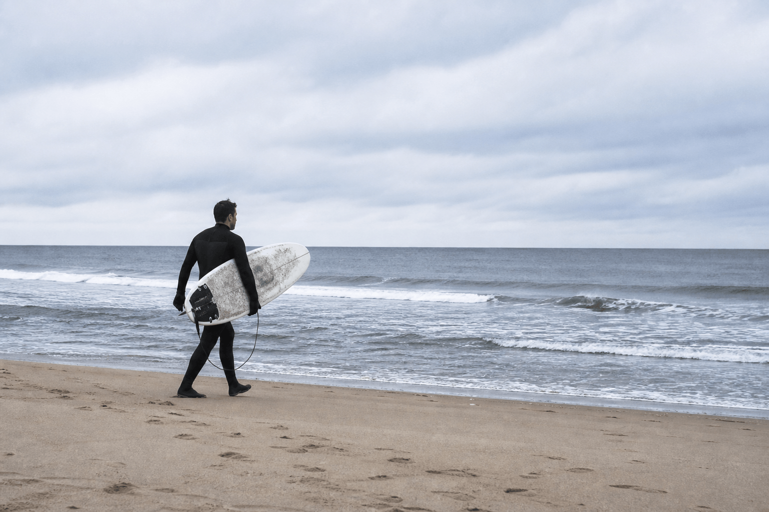 Winter surfing Ocean City Maryland: surfer in a wetsuit on a cold empty beach under gray-blue sky — Beach Blog photo