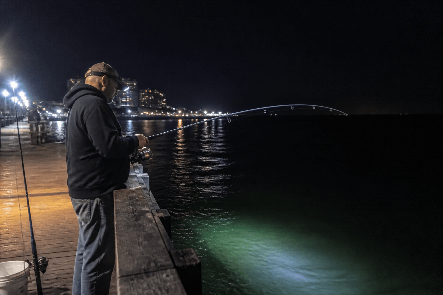 Angler night fishing on Ocean City pier under lights with dark Atlantic beyond